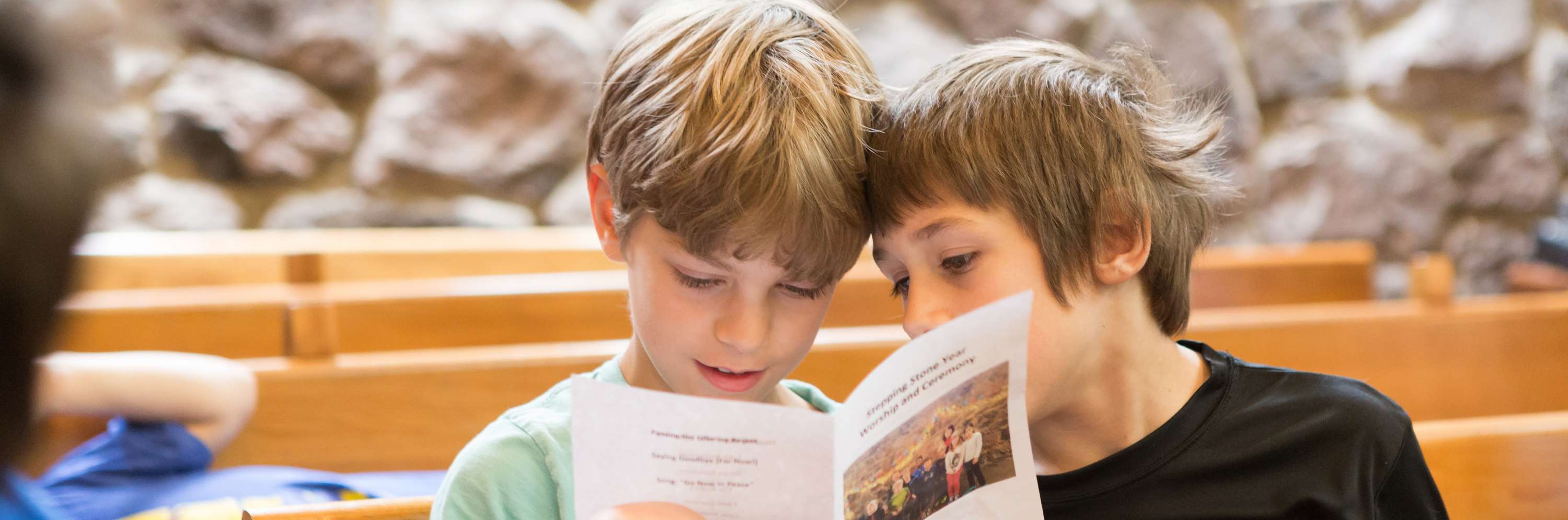 Two boys sitting in a pew reading a text